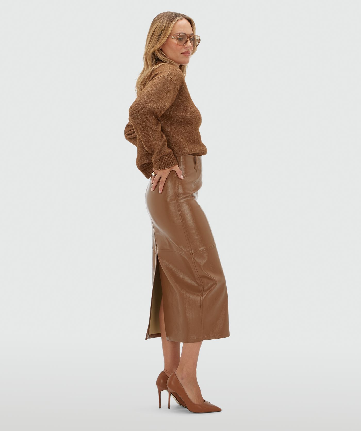 Model van opzij in een model in een lange lak look rok gecombineerd met een bruine trui.