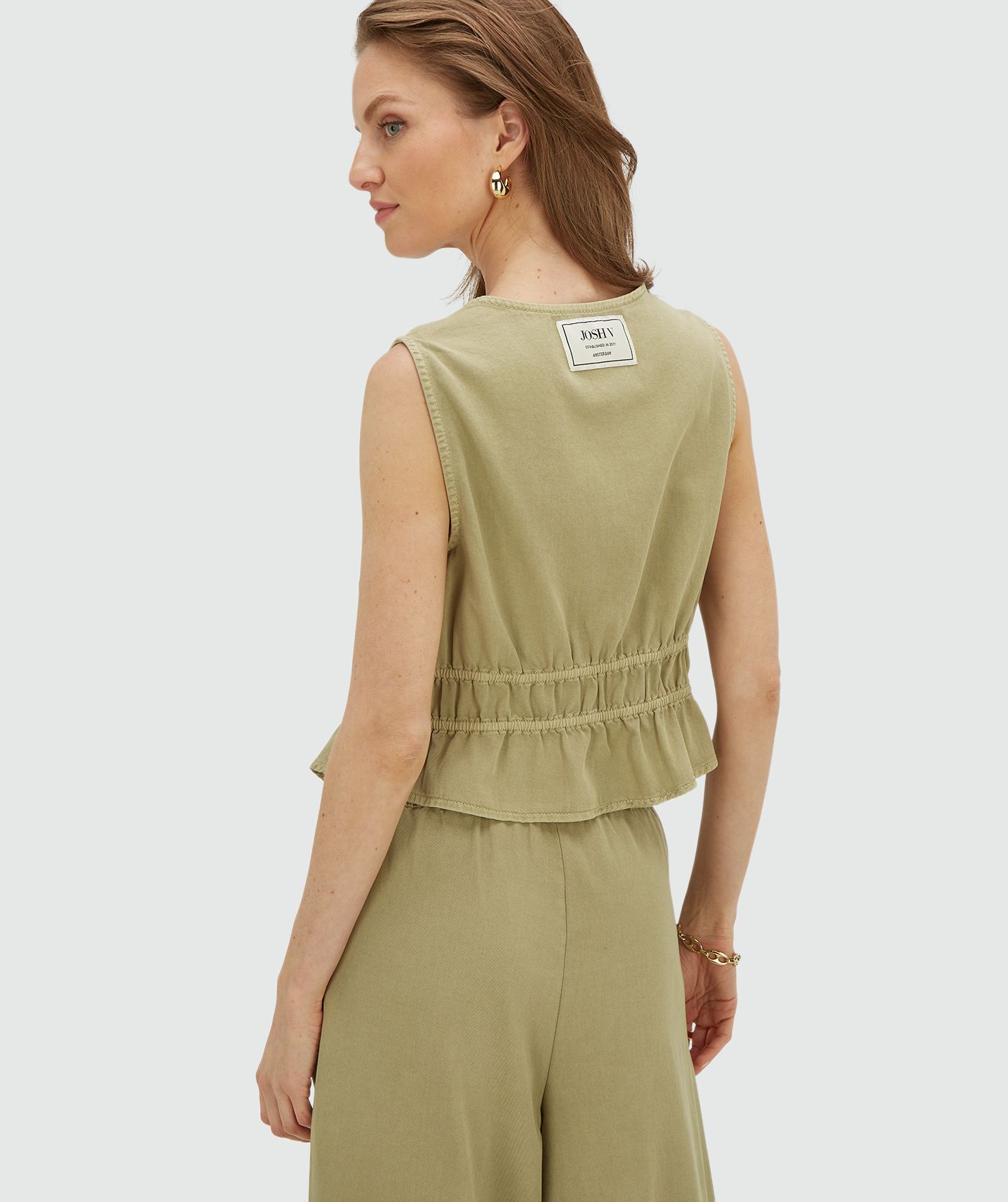 Achteraanzicht van een model in een getailleerde top met peplum in de kleur Dark Pistachio
