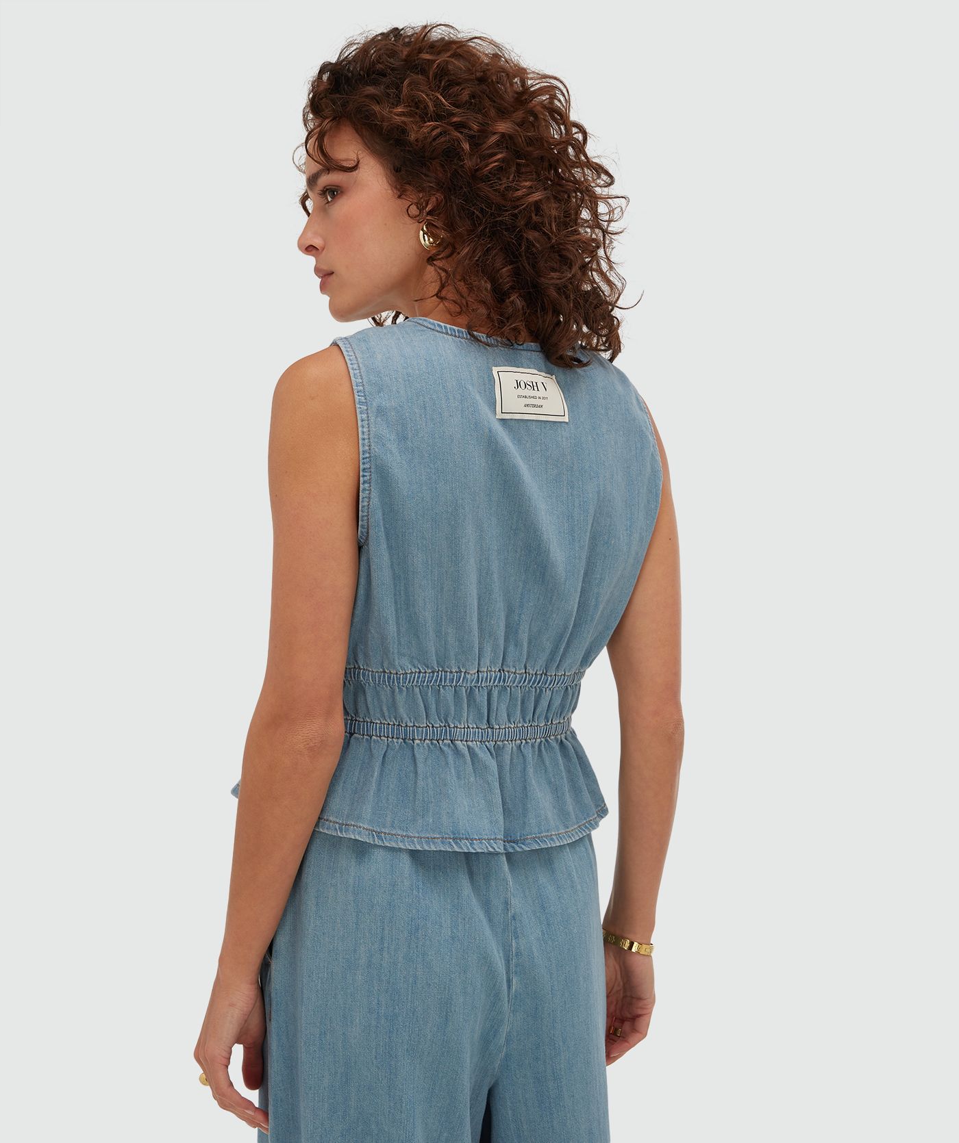 Achterzijde van een model in een getailleerde top met peplum in de kleur Mid Blue Denim