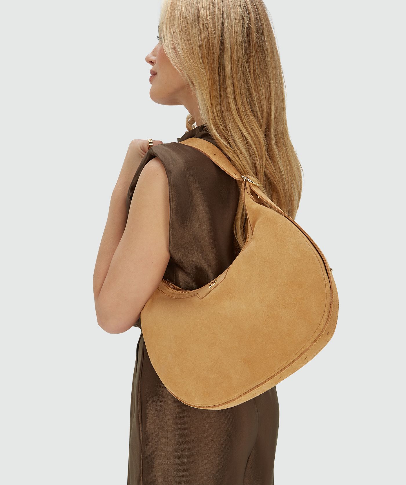 Het model draagt een suède tas in de kleur Light Camel verkort over haar linker schouder, voorzien van een ritssluiting en een verstelbaar hengsel