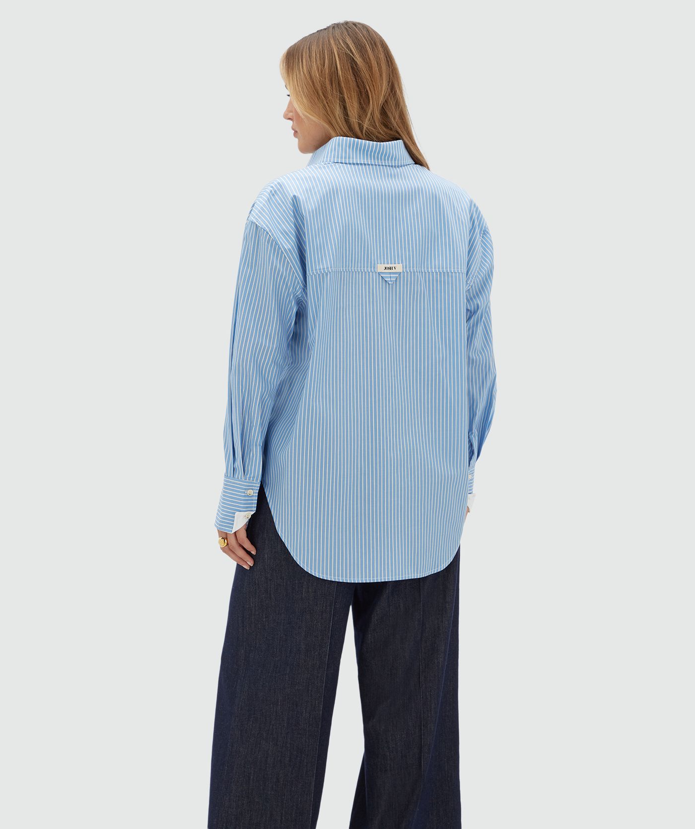 Achteraanzicht van een model in een lichtblauw met wit gestreepte blouse met en JOSH V label op de achterkant.