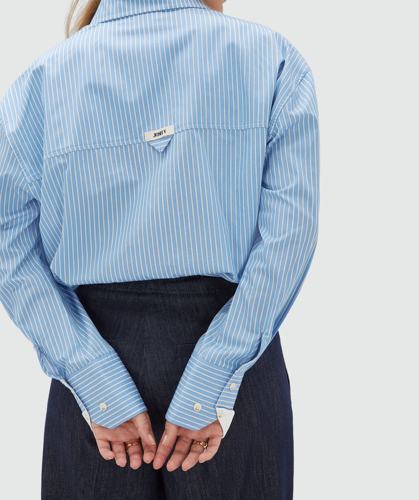 Achteraanzicht van een model in een lichtblauw met wit gestreepte witte blouse en heeft een JOSH V label.