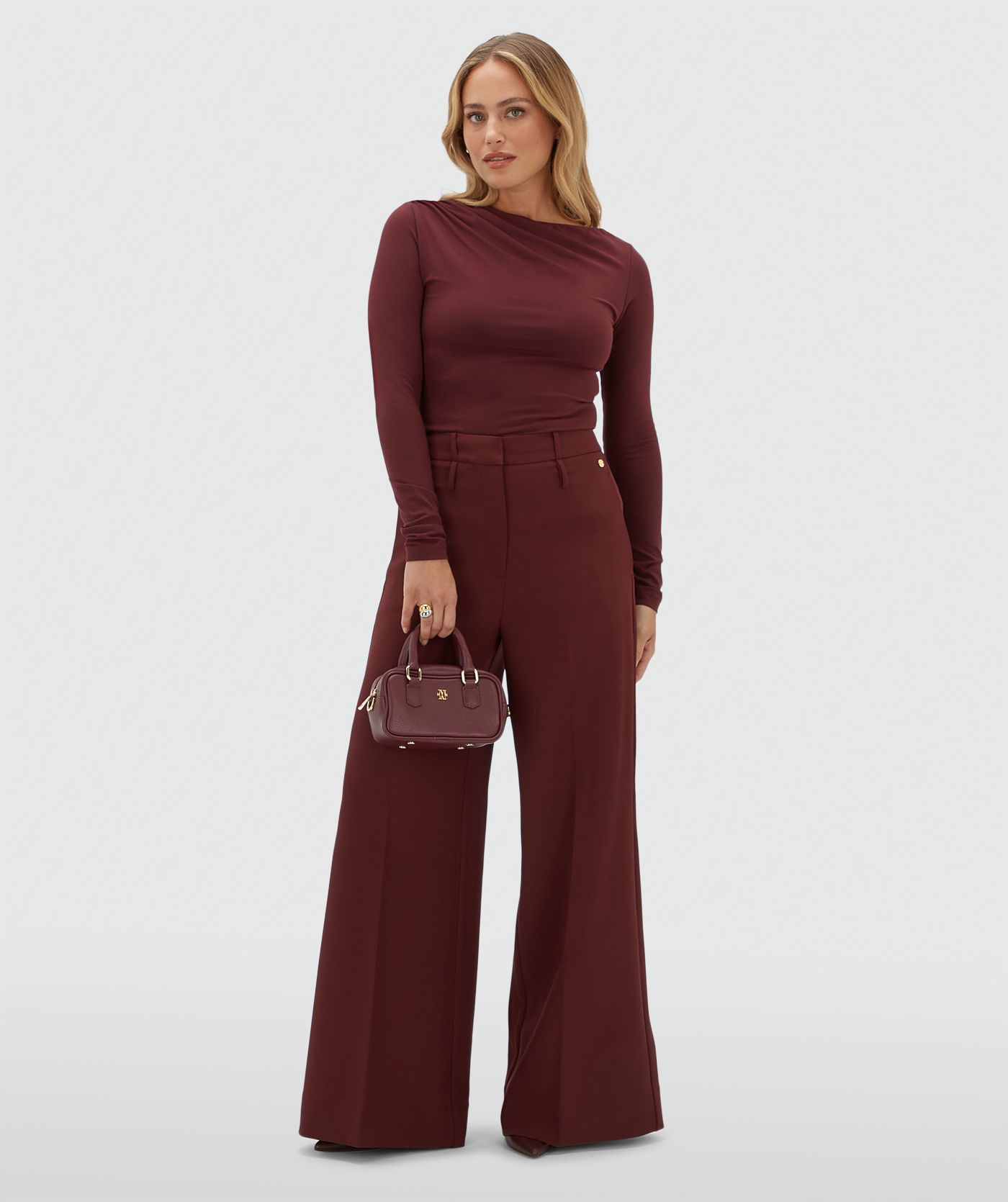Model draagt een donkerrode pantalon gecombineerd met een donkerrode top met lange mouwen.