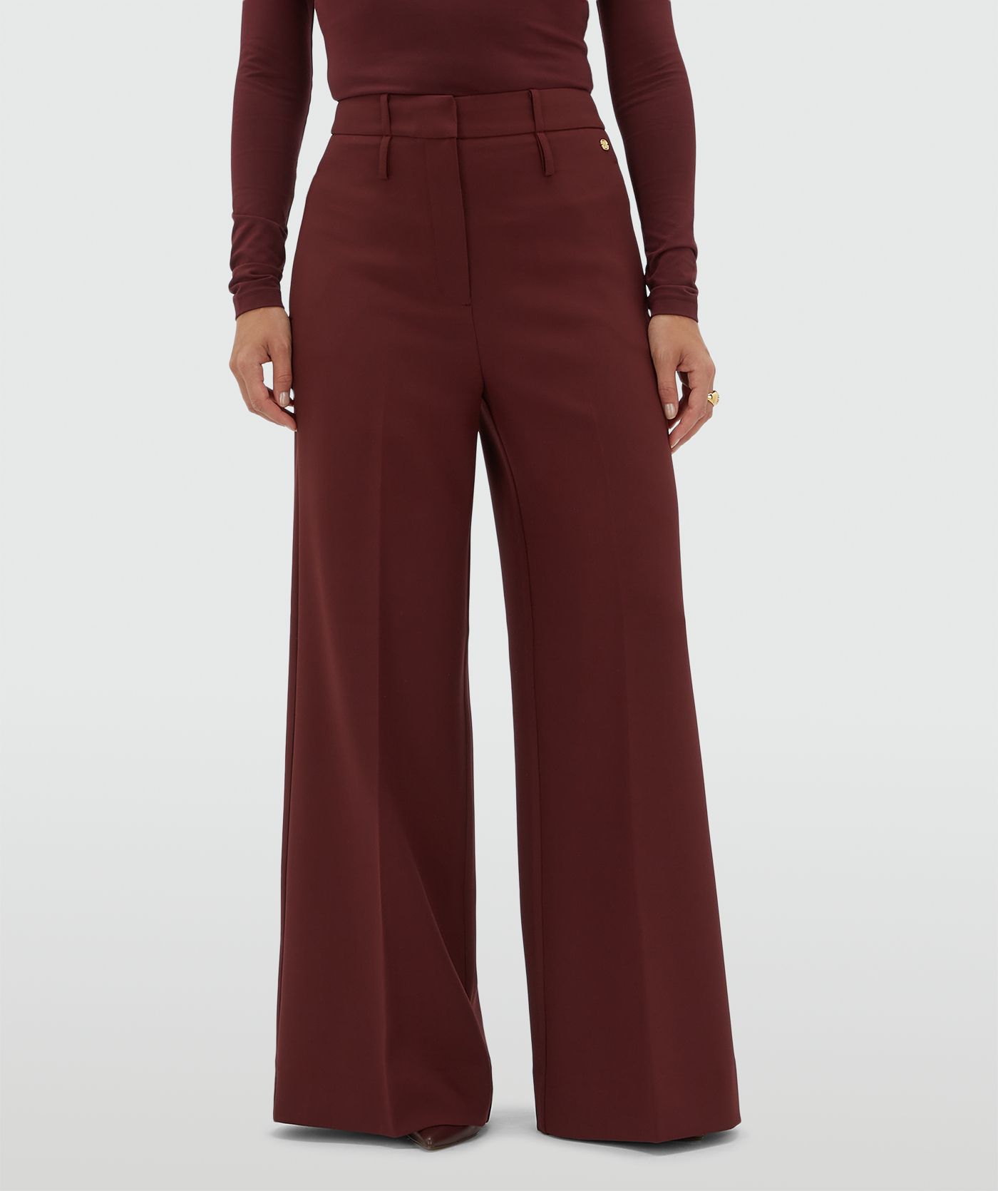 Model draagt een donkerrode pantalon gecombineerd met een donkerrode top met lange mouwen.