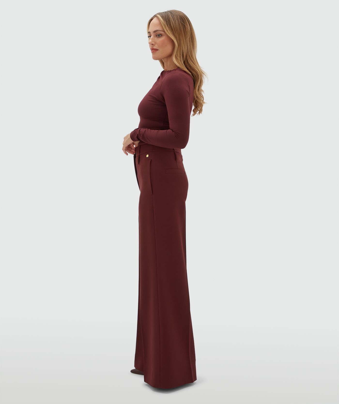 Model van opzij in een donkerrode pantalon gecombineerd met een donkerrode top met lange mouwen.