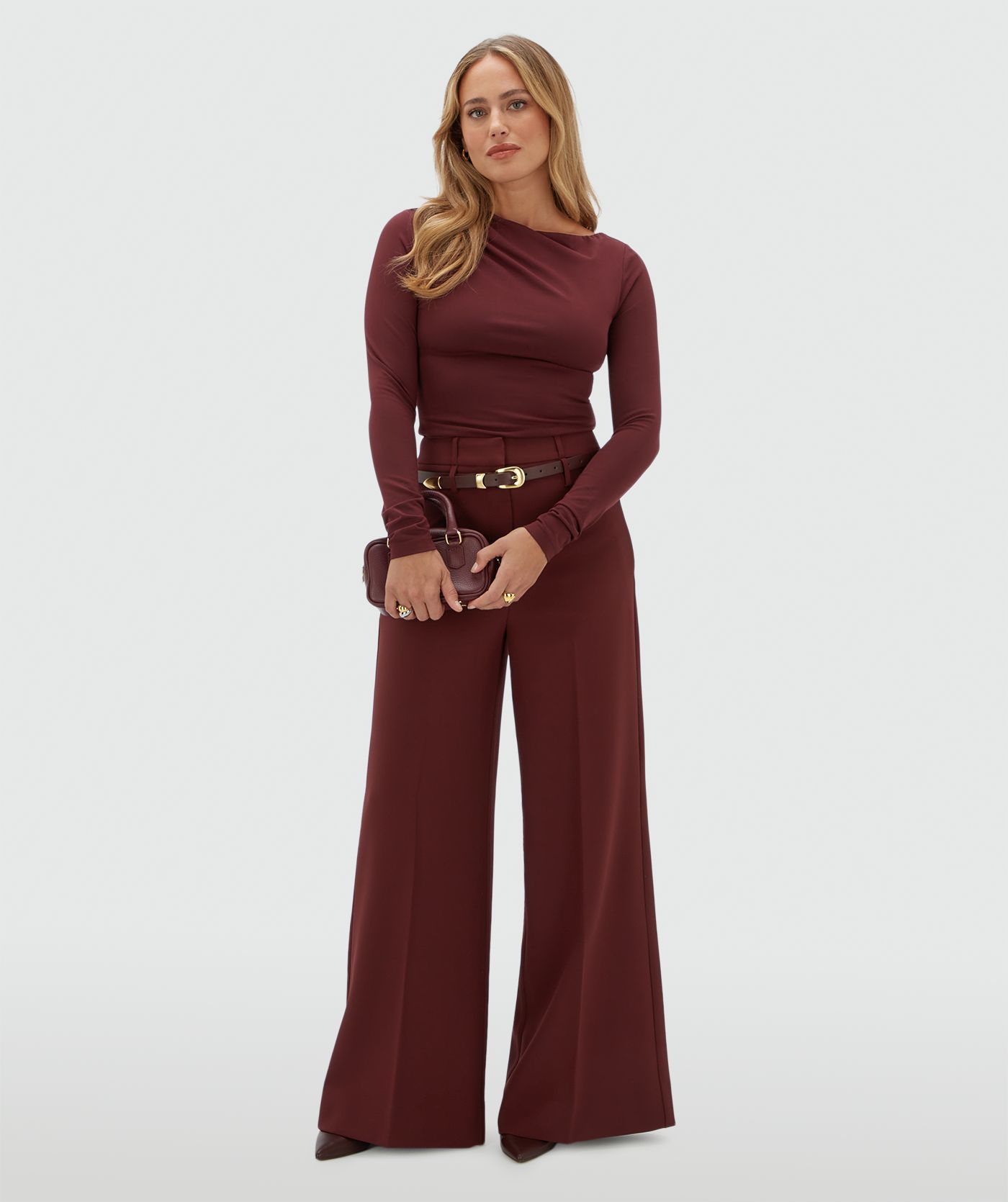 Model draagt een donkerrode pantalon gecombineerd met een donkerrode top met lange mouwen.