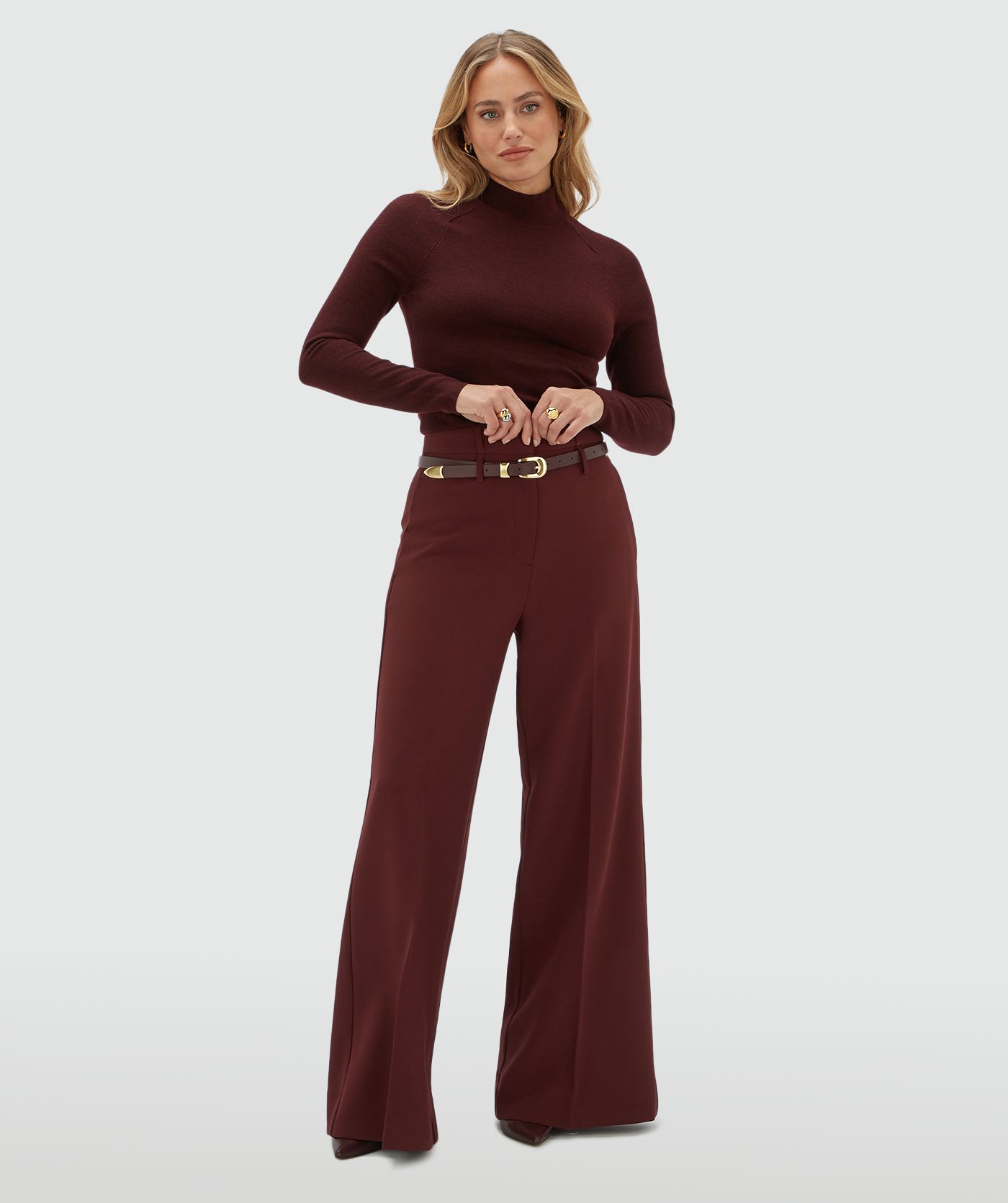 Model draagt een donkerrode coltrui gecombineerd met een donkerrode pantalon en een donkerrode riem.