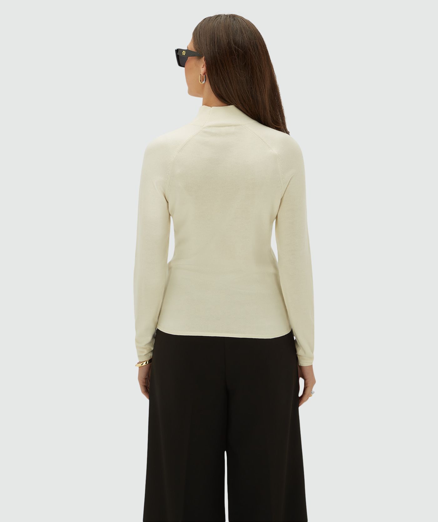 Achterzijde van model die een creme kleurige coltrui draagt, op een lichtgrijze achtergrond