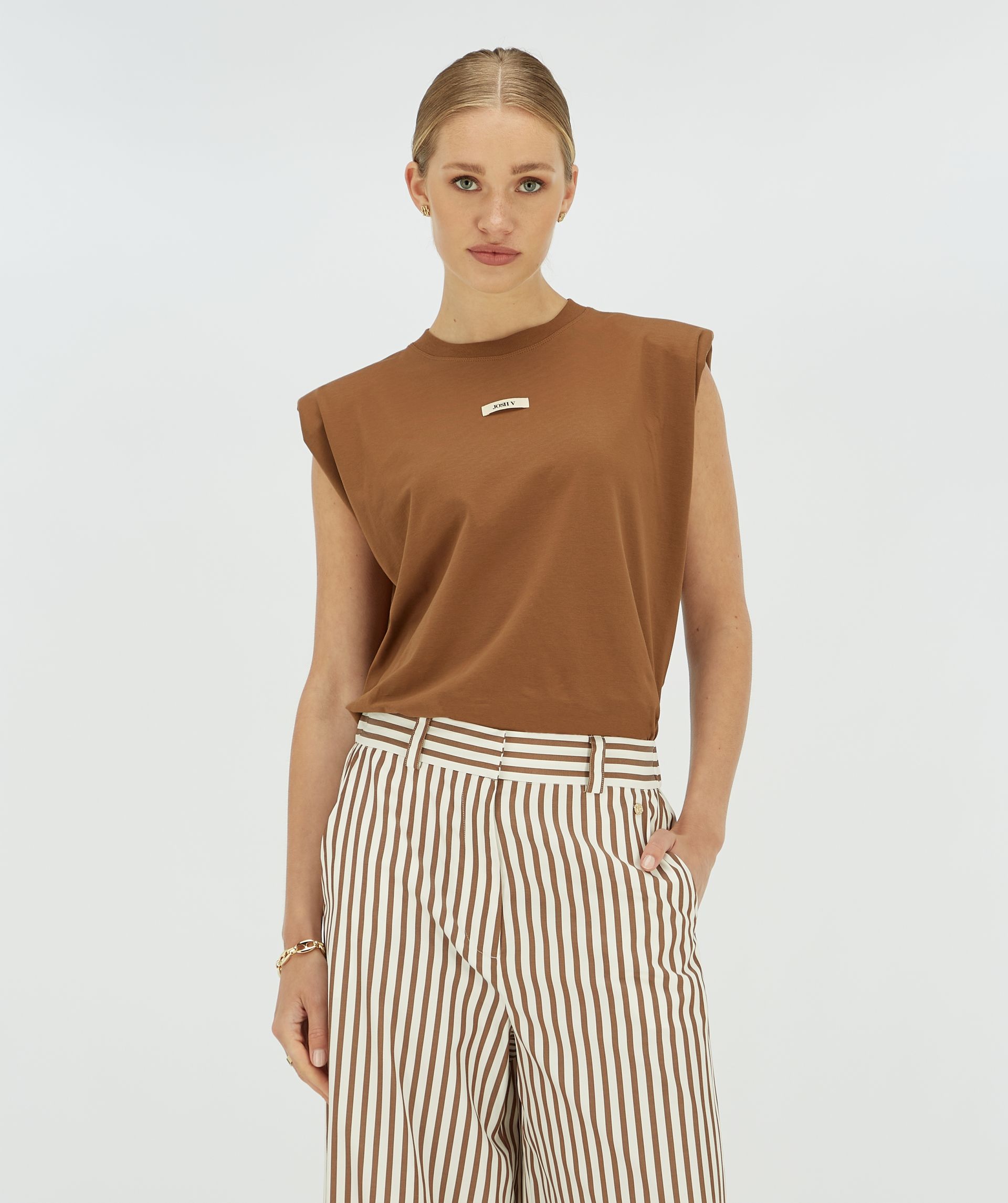 Model draagt een donkerbruin T-shirt met schoudervulling en een Josh v logo op de borst.