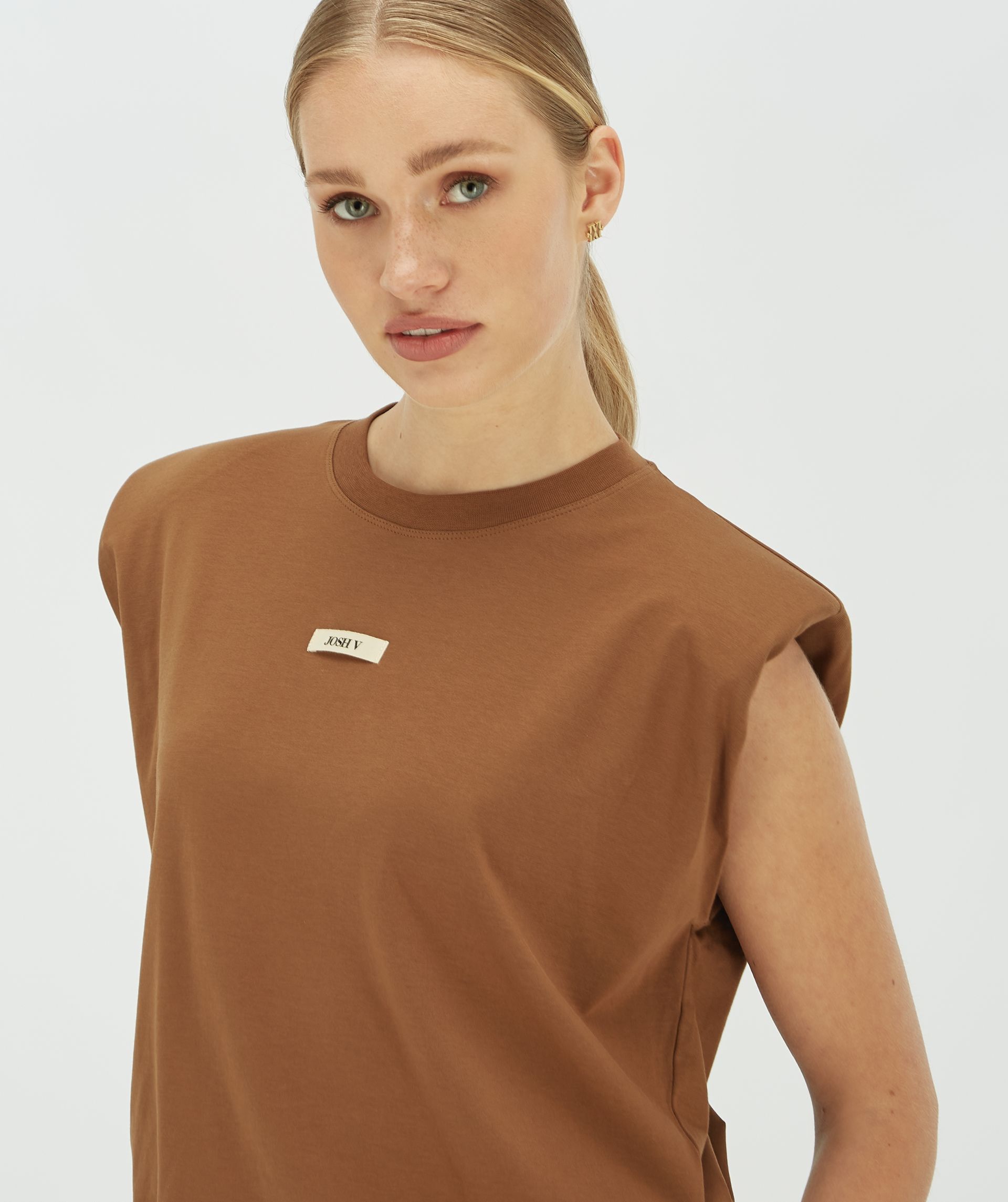 Model draagt een donkerbruin T-shirt met schoudervulling en een Josh v logo op de borst.