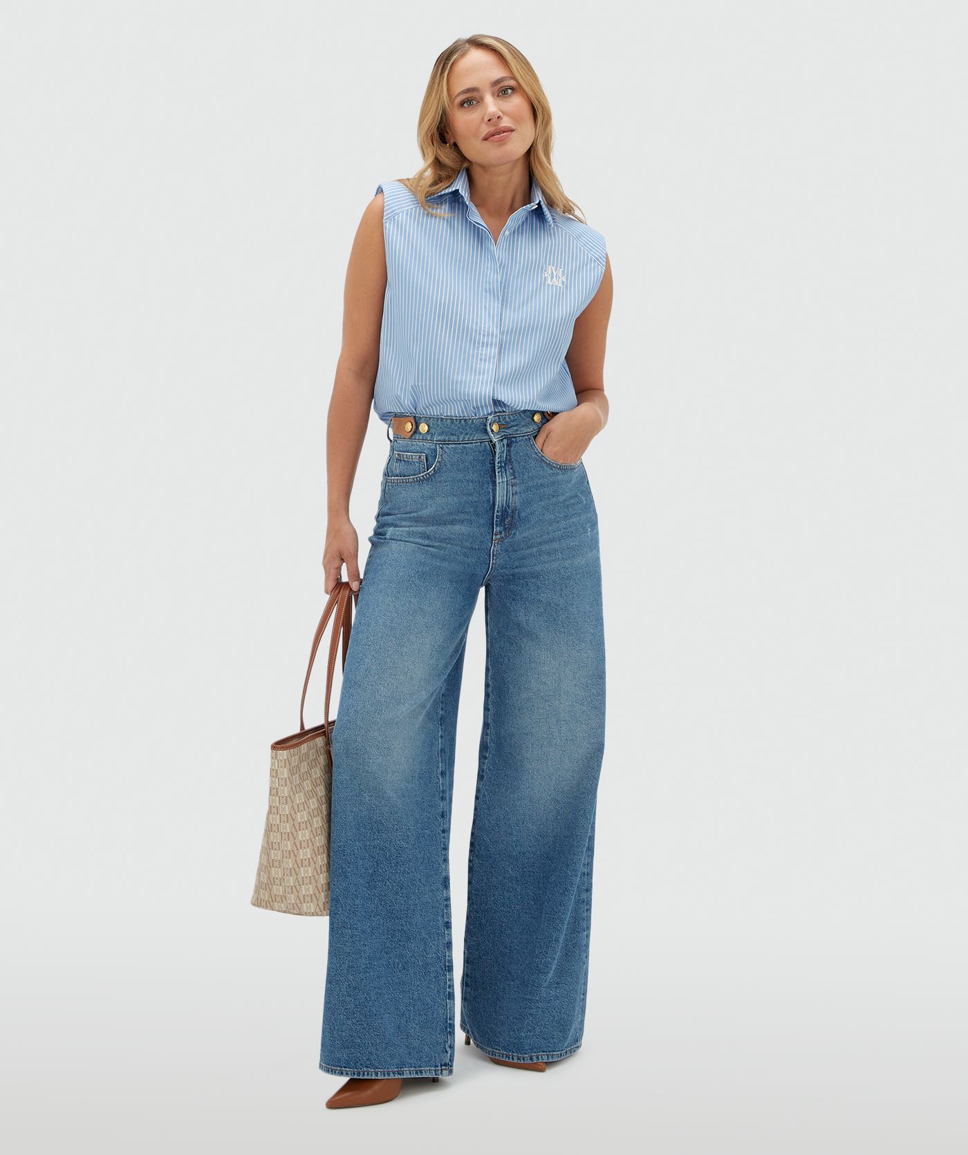Model draagt een lichtblauw wit gestreepte blouse zonder mouwen. De blouse is gecombineerd met een jeans.