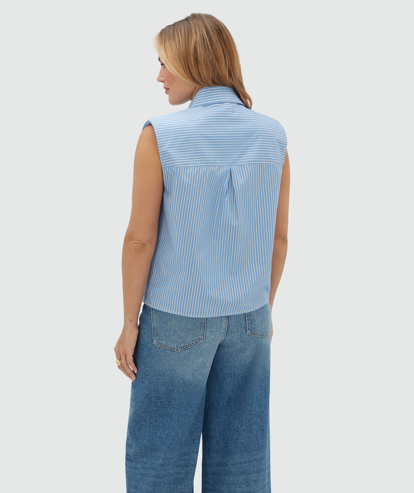 Achteraanzicht van een model in een lichtblauw wit gestreepte blouse zonder mouwen.