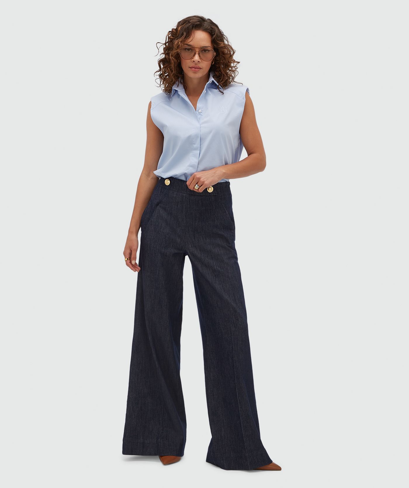 Model draagt een lichtblauwe blouse zonder mouwen.