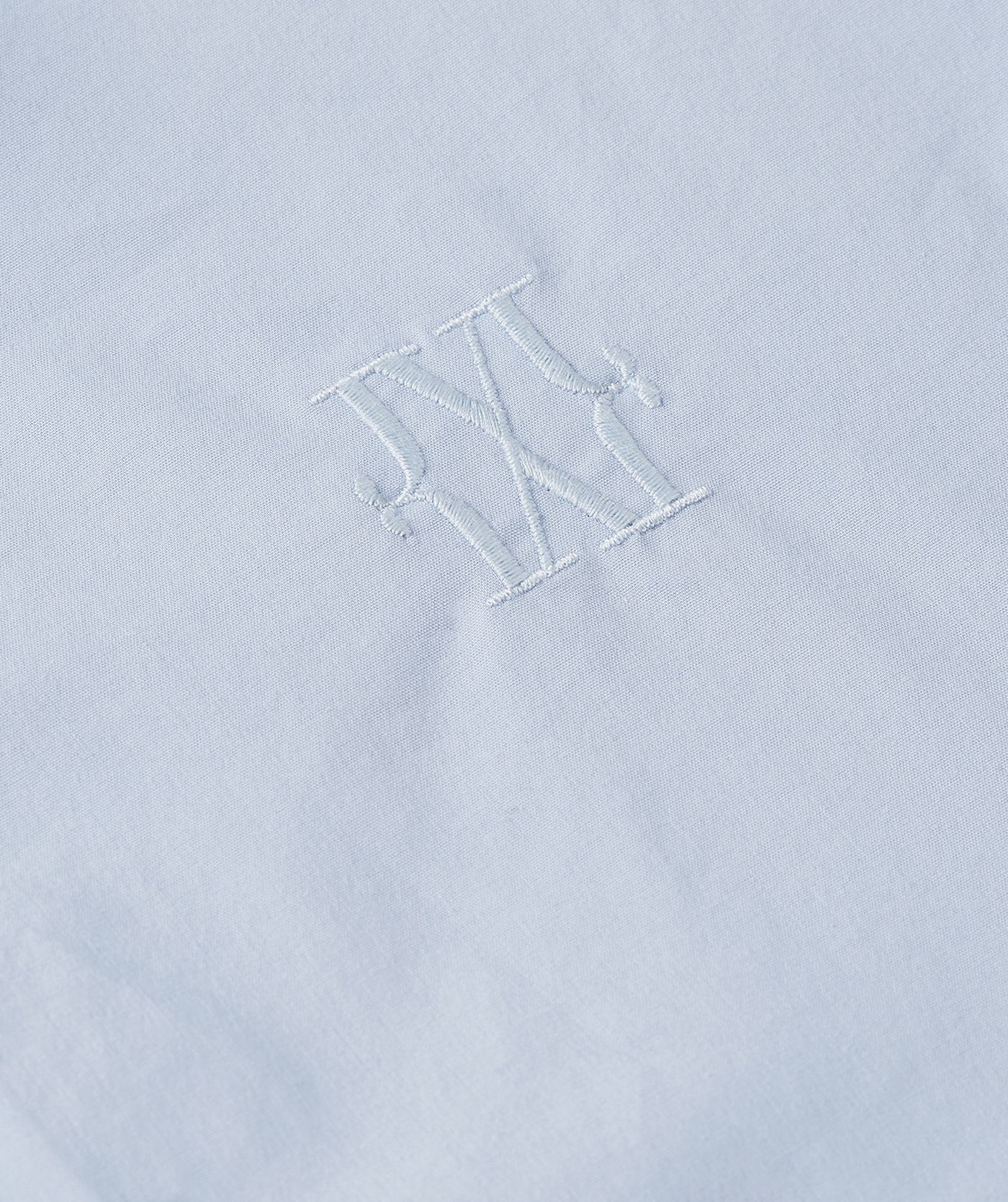 Close-up van het logo dat op de borst zit van de lichtblauwe blosue.