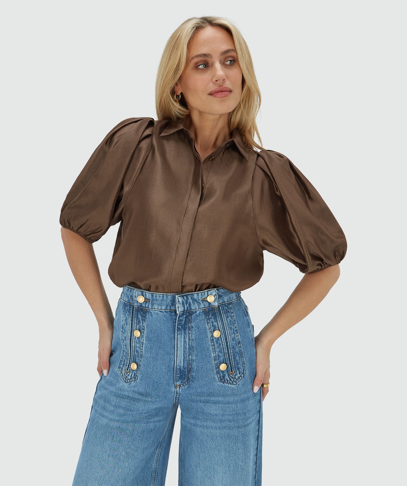 Het model draagt een regular fit blouse van een glanzende bruine stof, afgewerkt met een strikdetail bij de halslijn
