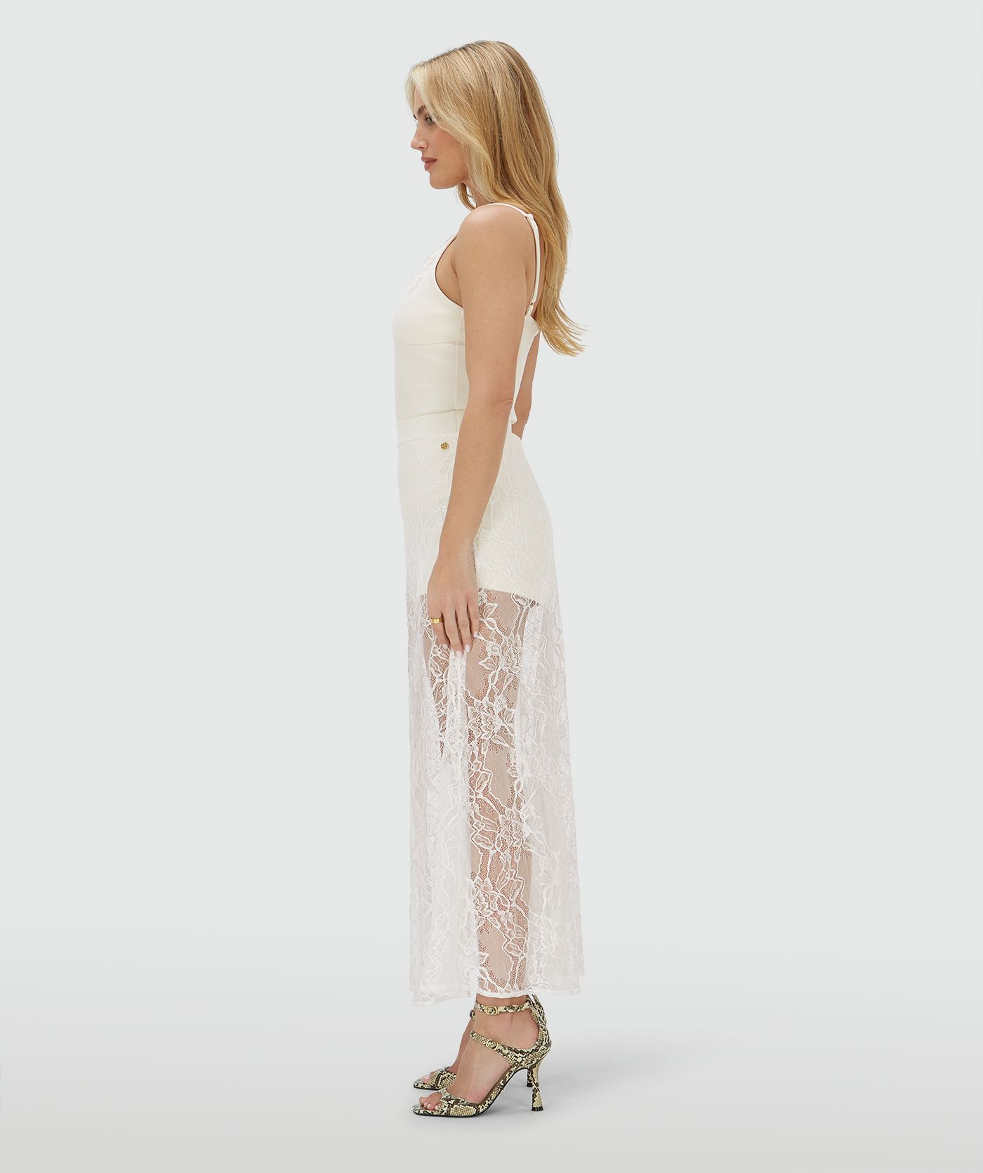Zijaanzicht van een model in een high waisted kanten rok in de kleur Crème Wit, met een jersey broekje eronder. In het midden van de elastische tailleband is het JOSH V-label zichtbaar