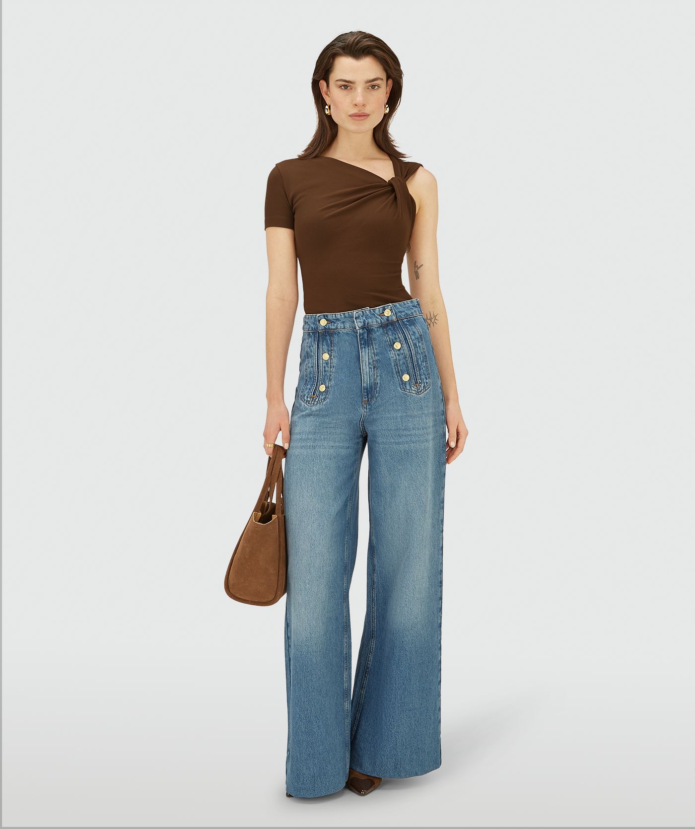 Model draagt een bruine, asymmetrische top met korte mouw, schuin halsdetail en knoopdetail op de schouder