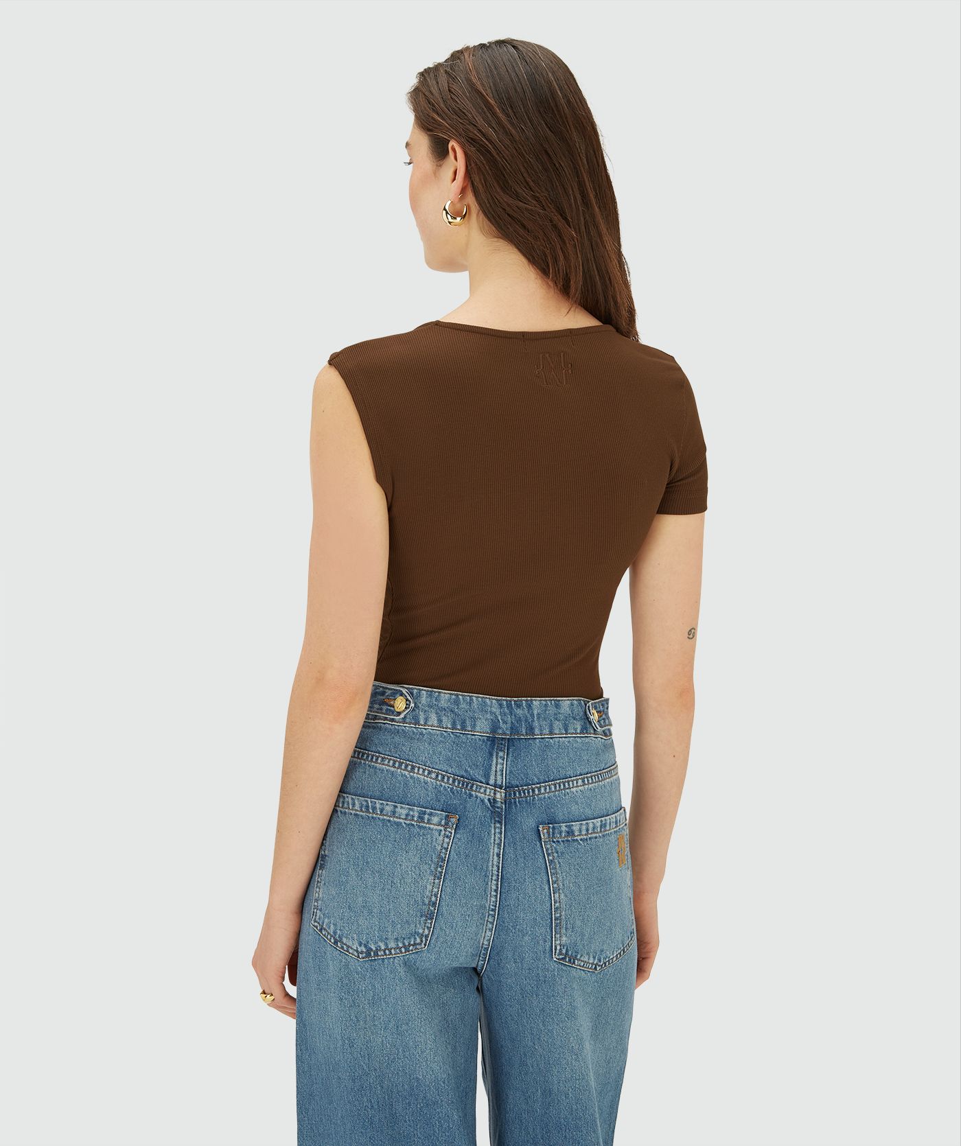 Achteraanzicht van model in een bruine, asymmetrische top met korte mouw, schuin halsdetail en knoopdetail op de schouder