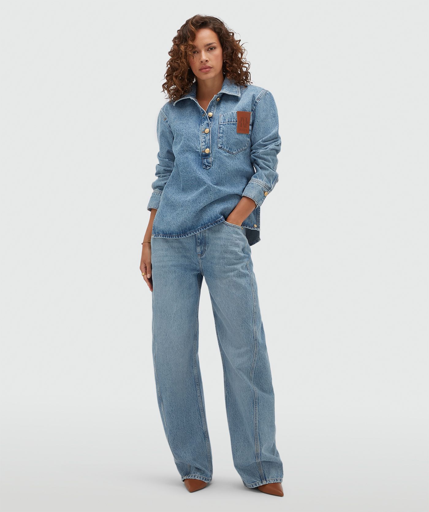 Model draagt een oversized denim blouse met een JV embleem. 