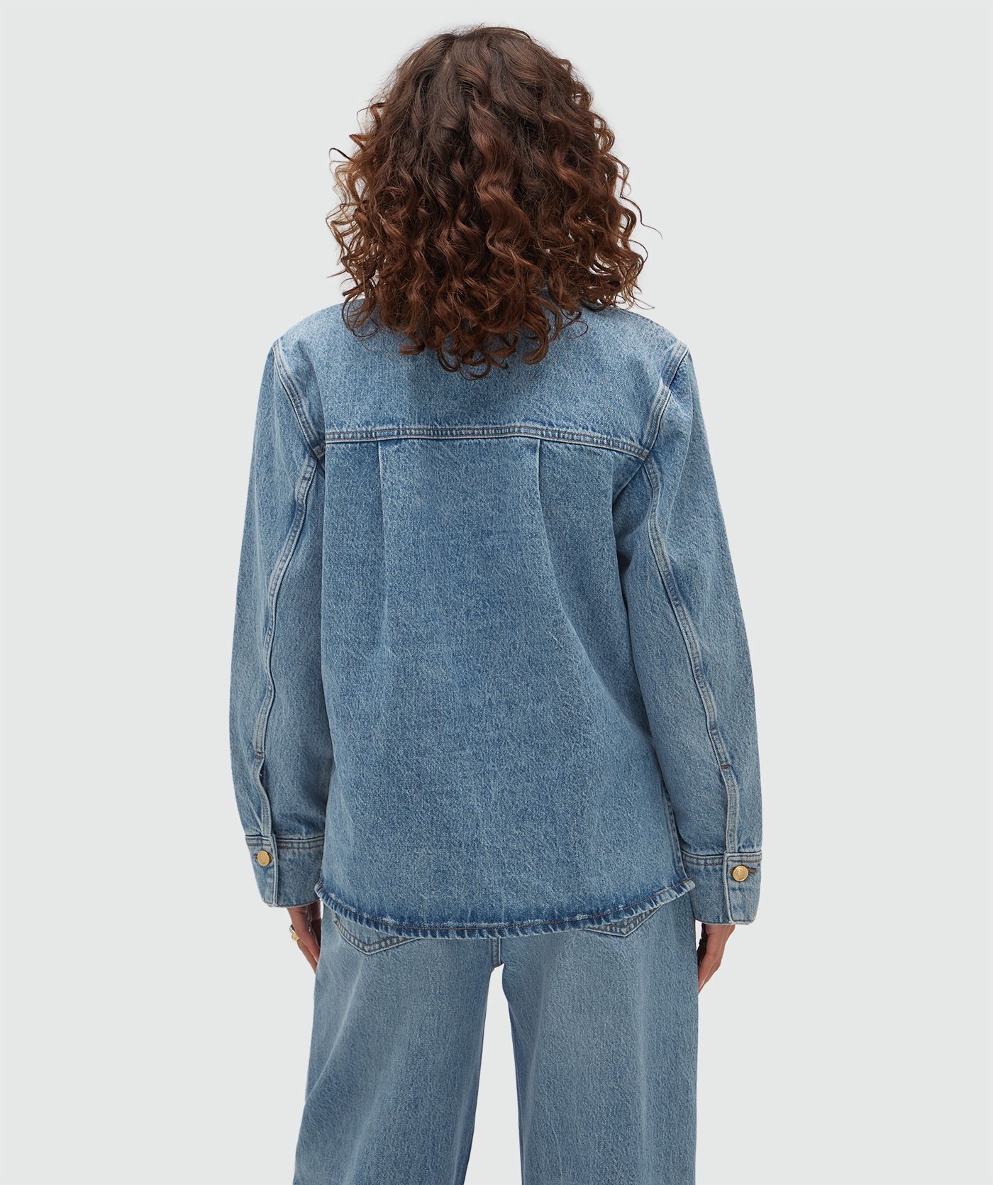 Achteraanzicht van een model in een oversized denim blouse. 