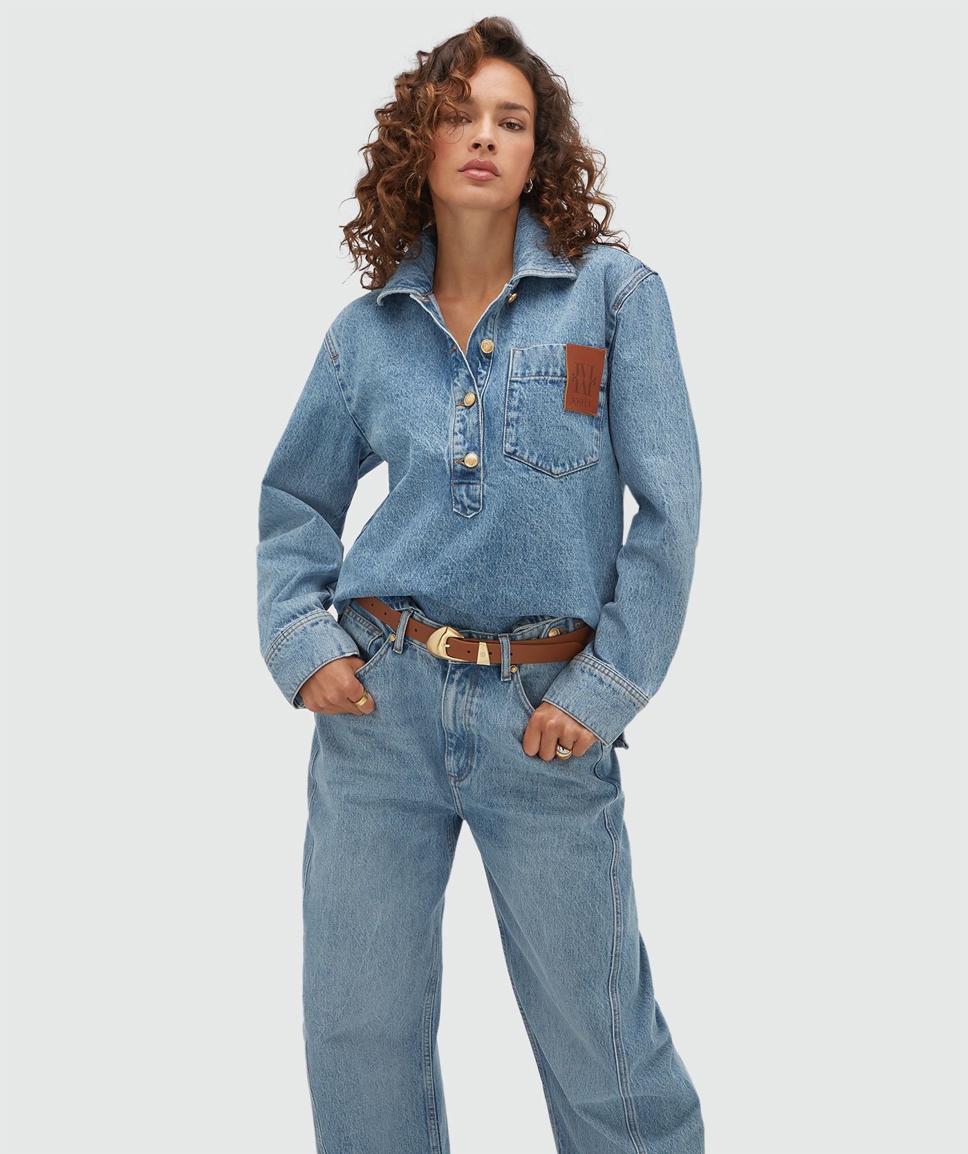 Model draagt een oversized denim blouse met een JV embleem. 