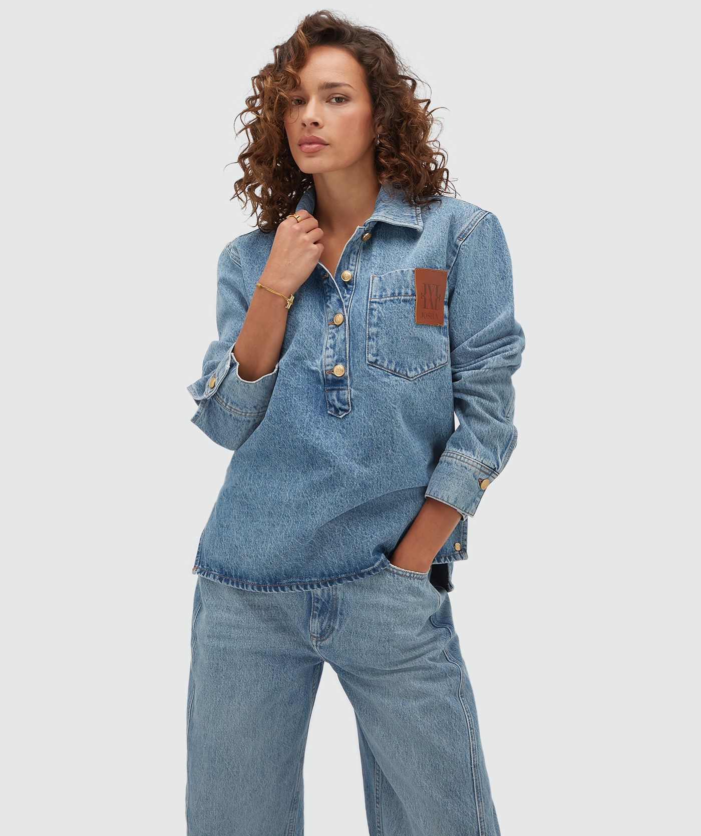 Model draagt een oversized denim blouse met een JV embleem. 
