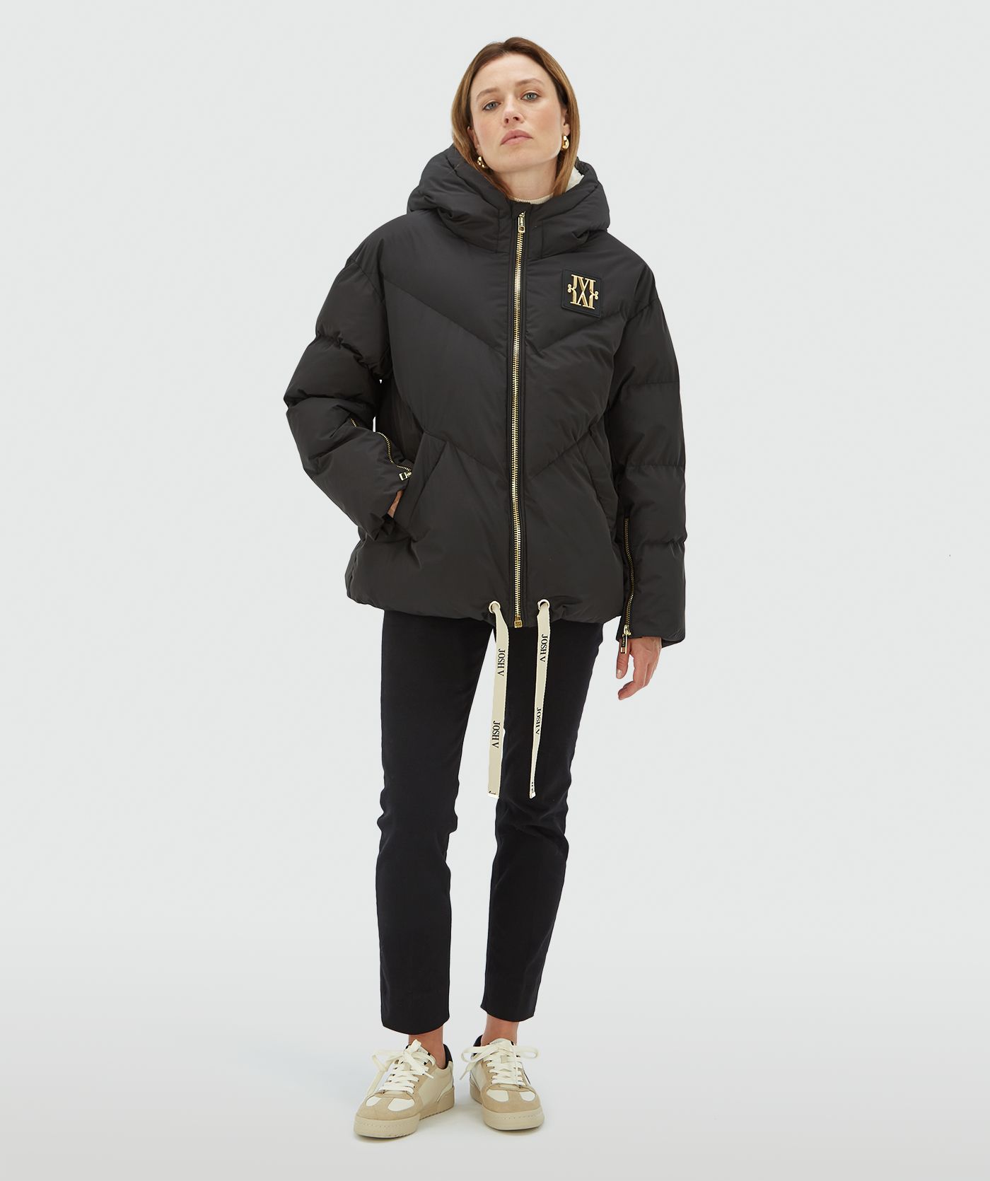 Model draagt een zwarte oversized gewatteerde jas met JOSH V branded trekkoord aan de onderkant, capuchon, goudkleurige ritssluiting en rubberen patch op de borst - Josh V