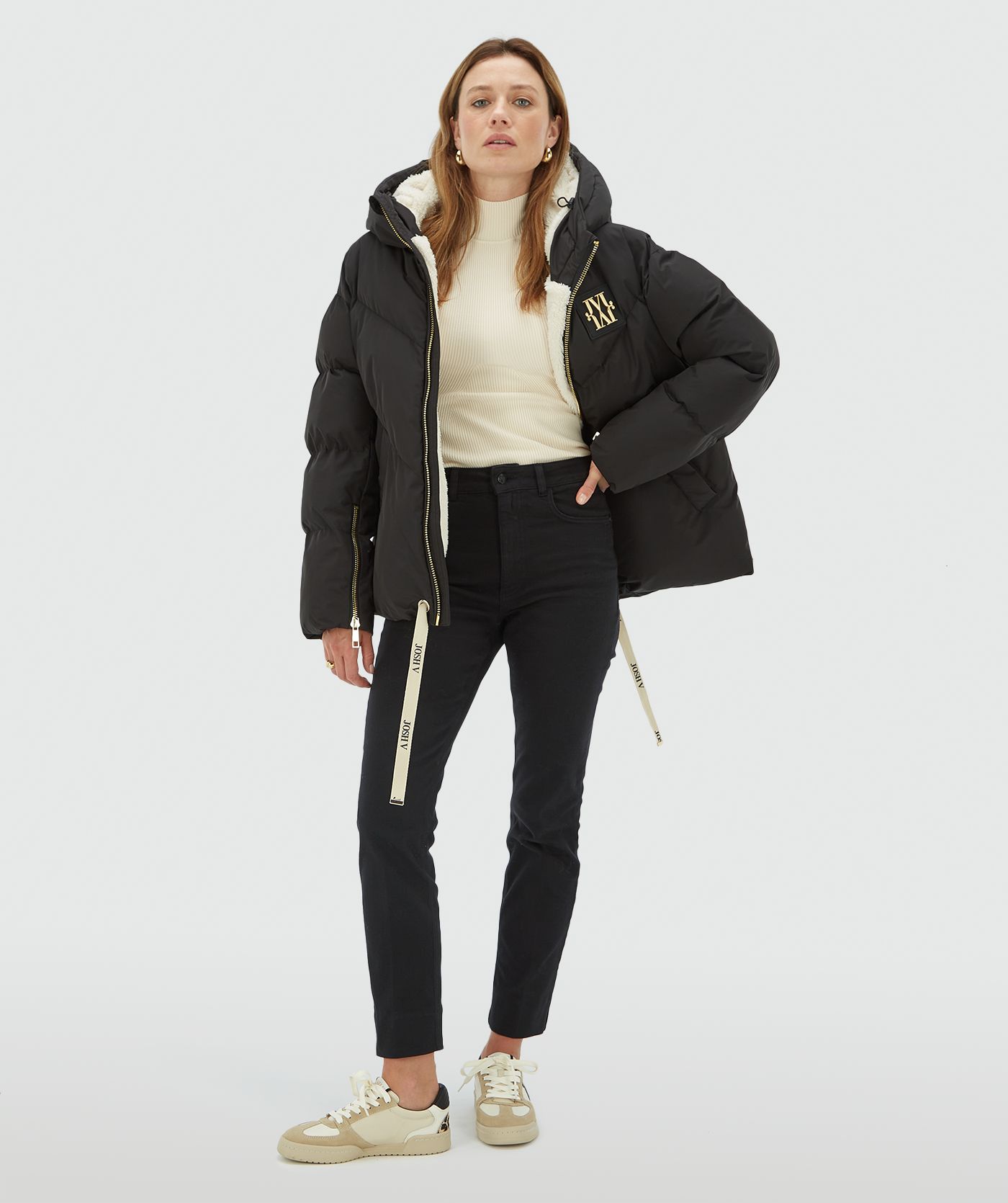 Model draagt een zwarte oversized gewatteerde jas met JOSH V branded trekkoord aan de onderkant, capuchon, goudkleurige ritssluiting en rubberen patch op de borst - Josh V