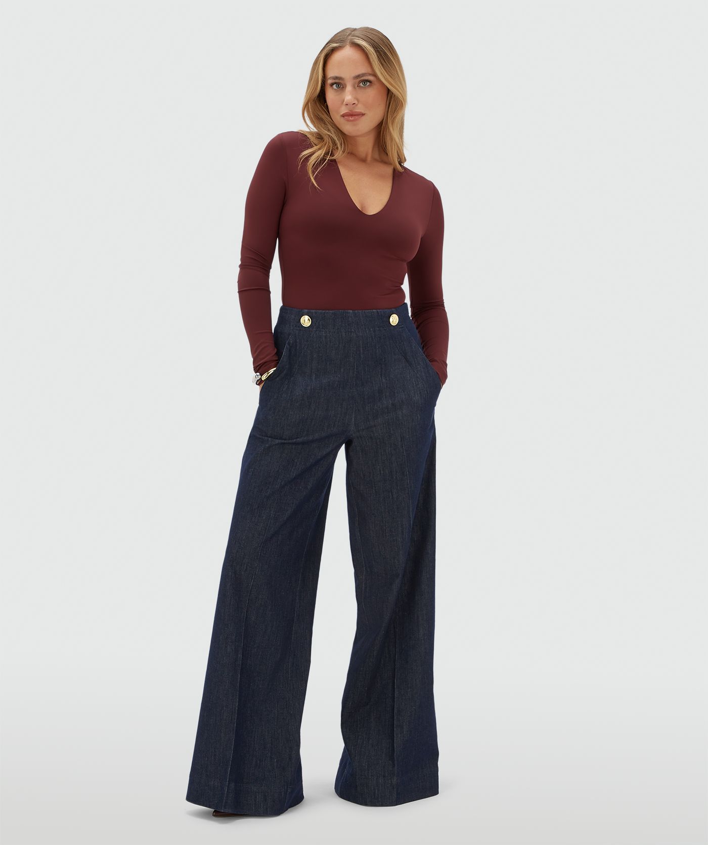 Model draagt een donkerrode body met v-hals gecombineerd met een donkerblauwe pantalon.