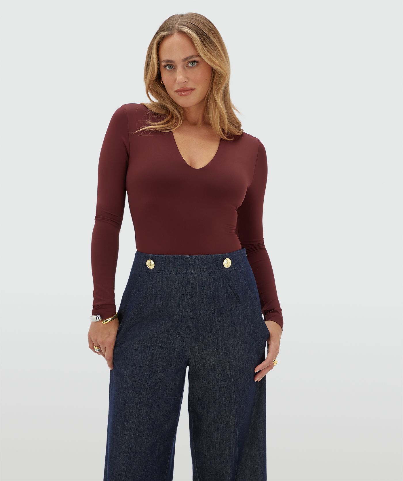 Model draagt een donkerrode body met v-hals gecombineerd met een donkerblauwe pantalon.
