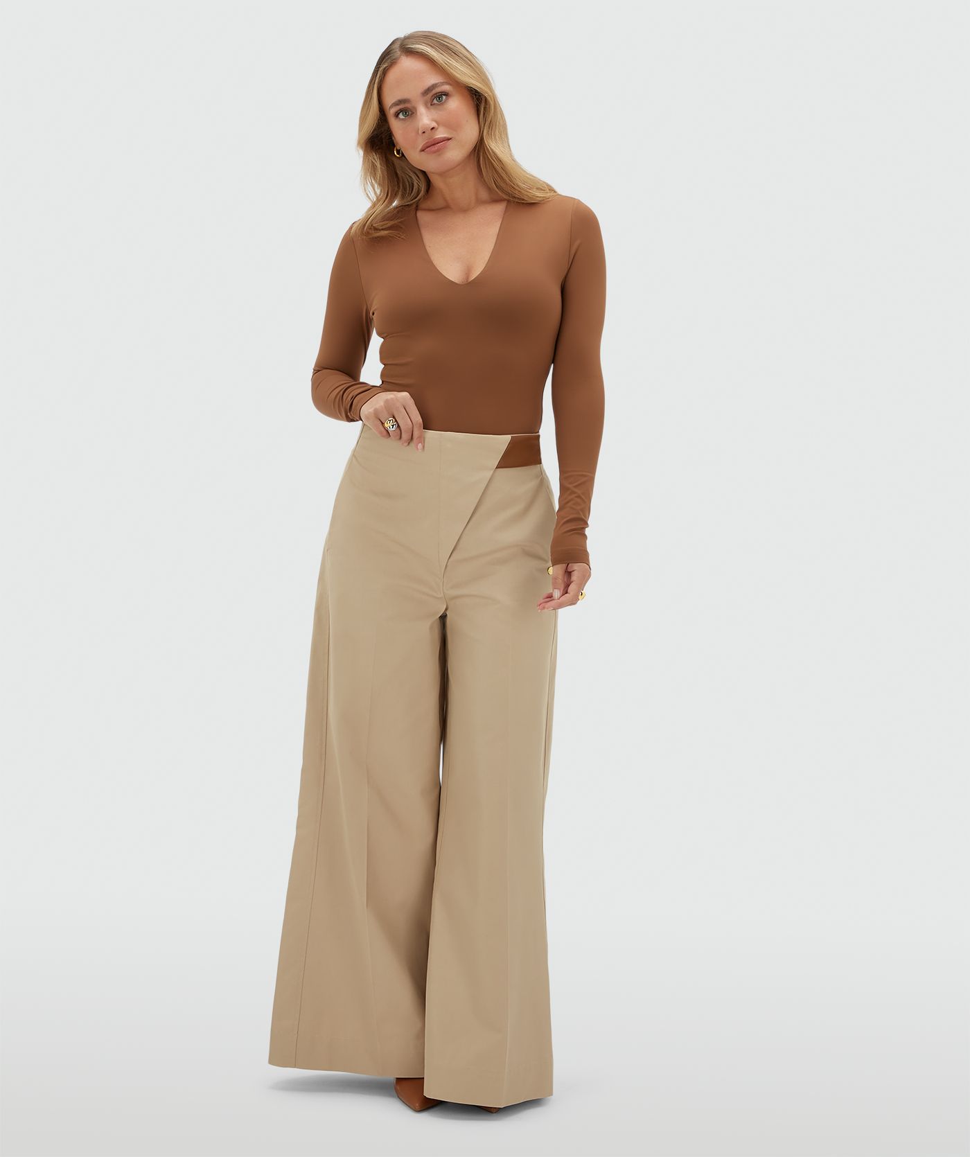 Model draagt een lichtbruine body met een v-hals gecombineerd met beige broek.