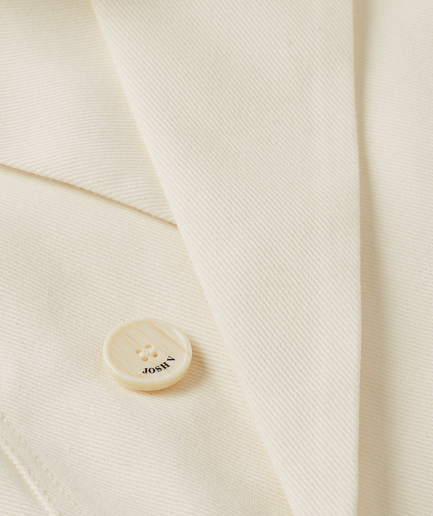 Close-up van JOSH V-knopen die op de crème blazer zitten.