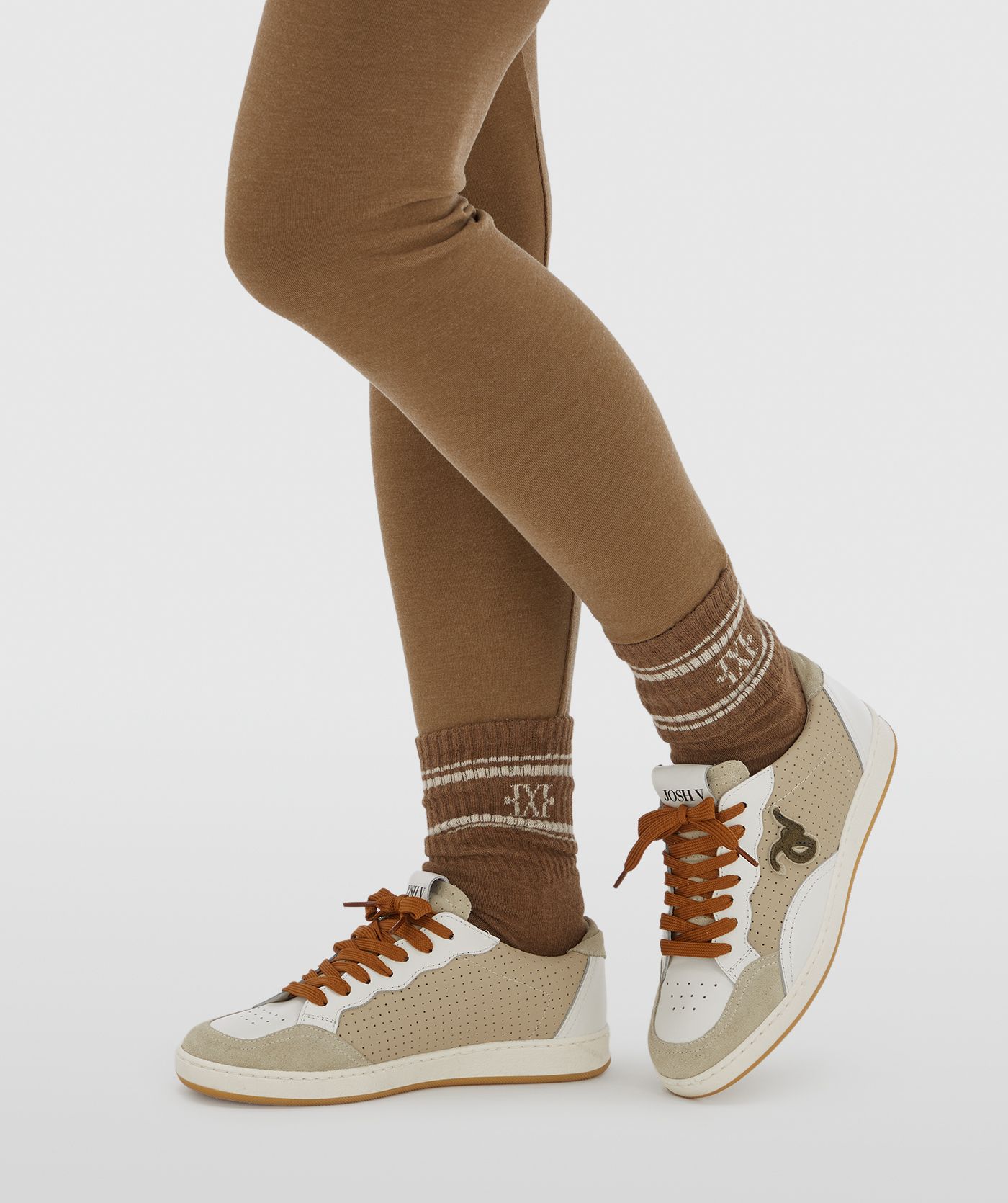 Model draagt beige sneakers met een groene touch inclusief bruine veters. 