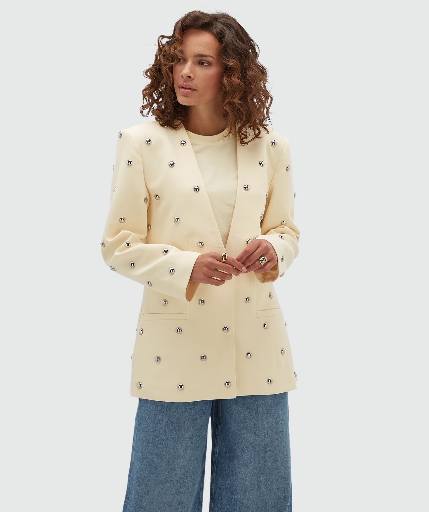 Model draagt lichtgele blazer met zilveren studs.